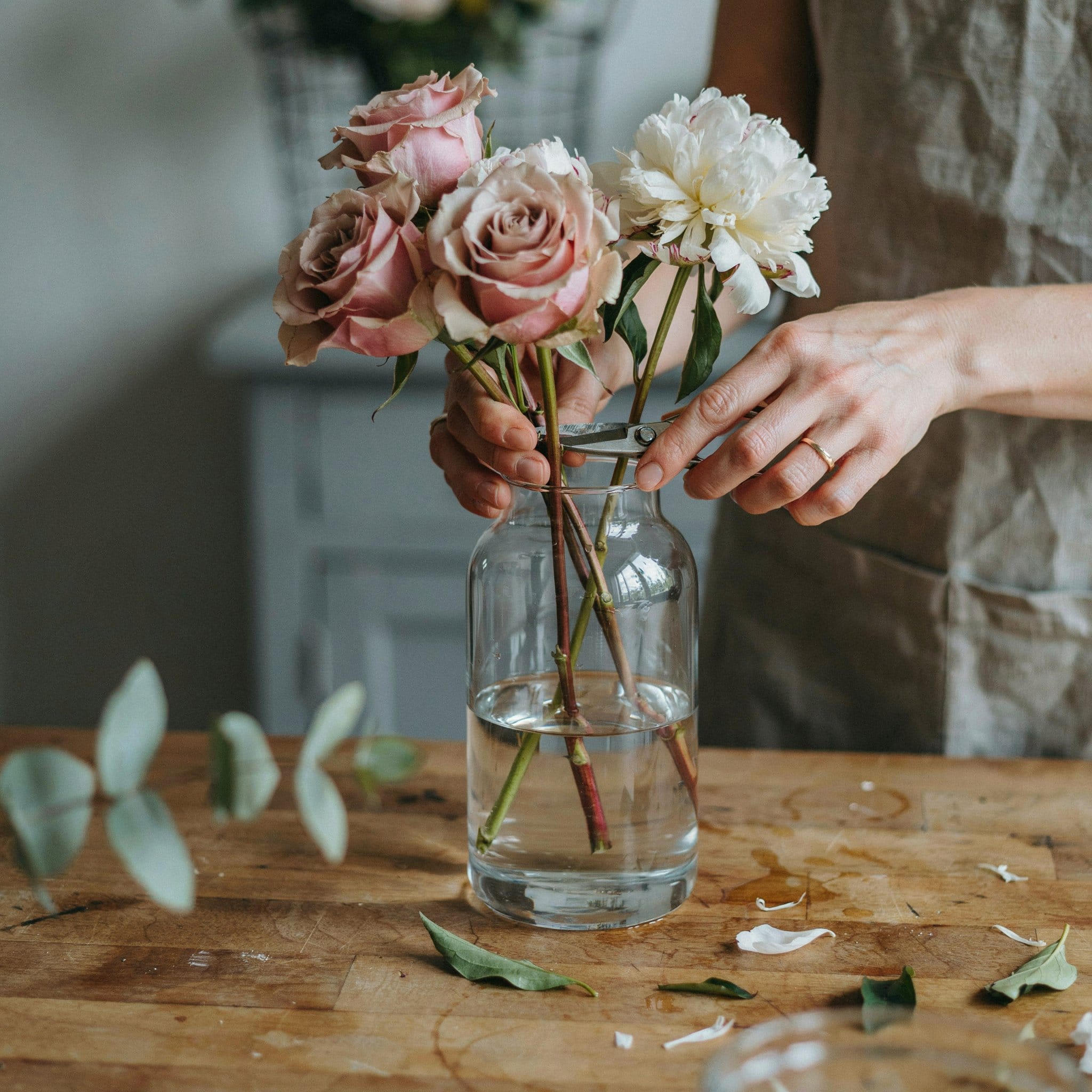 Close-up of hands trimming and arranging fresh roses and peonies into a glass vase